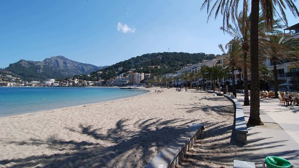 Une plage offrant une vue dégagée sur la mer, une montagne en arrière-plan et une rangée de bâtiments le long de la côte.