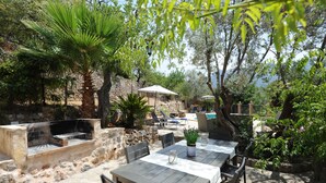 Une terrasse extérieure avec des murs en pierre, un barbecue et une table dressée pour les repas.