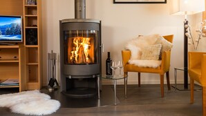 A cozy living room with a wood-burning stove, a television, and a comfortable armchair. - Duplex Penthouse in Chalet Luna (Wengen)