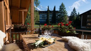 A wooden deck with a table set for a meal, surrounded by potted plants and flowers. - Duplex Penthouse in Chalet Luna (Wengen)