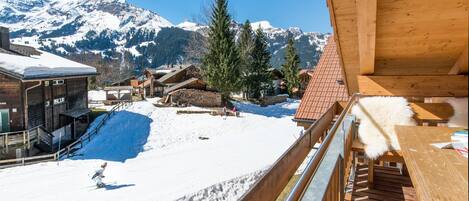 Una cabaña de madera con una pista de esquí al fondo y montañas cubiertas de nieve.