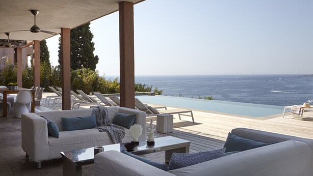 Ein Außenbereich mit Sitzgelegenheit, Pool und Meerblick, ausgestattet mit einer Couch, Stühlen und einem Tisch.