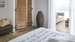 Ein Schlafzimmer mit einem Bett, einem Holzschrank, einer großen Vase und Meerblick durch ein Fenster.