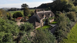 A traditional stone house with a thatched roof, surrounded by lush greenery and a well-maintained lawn. - Orchard Cottage - sleeps 8 guests  in 4 bedrooms (Ilminster)