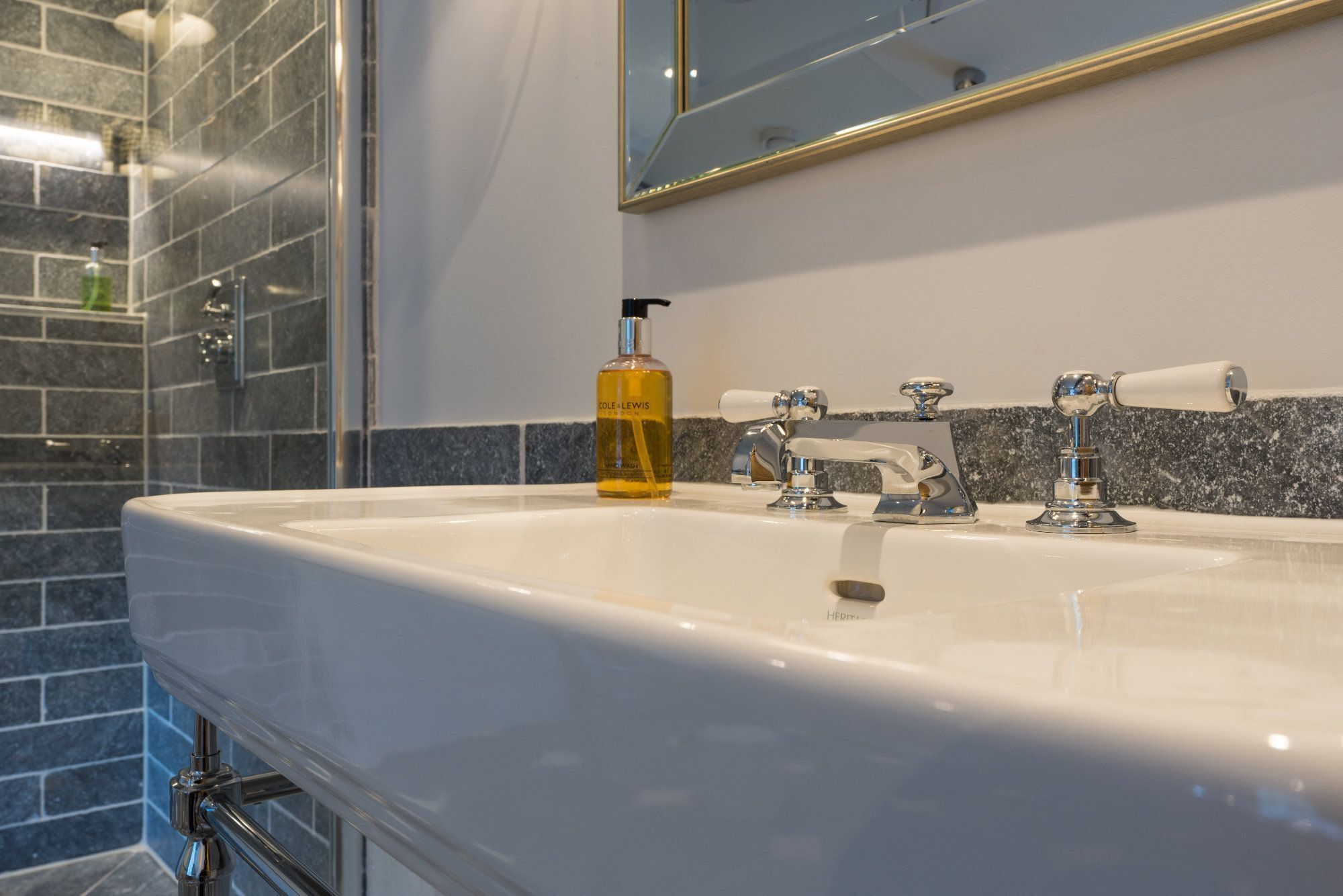 Une salle de bain avec un lavabo blanc, deux robinets, un miroir et un flacon de savon.