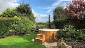 A hot tub in a garden with a stone pathway leading to it, surrounded by lush greenery and a clear sky. - Orchard Cottage - sleeps 8 guests  in 4 bedrooms (Ilminster)