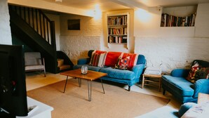 A cozy living room with a blue sofa, a wooden coffee table, and a bookshelf against a white brick wall. - Apple Cottage - A stylish country retreat, it's the ideal getaway. (Wimborne)