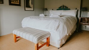 A neatly made bed with white linens, a wooden bench, and two framed pictures on the wall. - Apple Cottage - A stylish country retreat, it's the ideal getaway. (Wimborne)