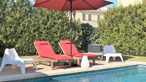Une piscine avec des chaises longues rouges et blanches et un tabouret blanc.