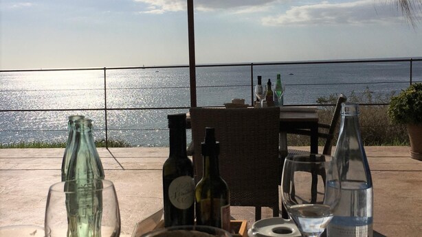 Un espace extérieur aménagé pour prendre les repas, avec vue sur la mer, comprenant une table ornée de bouteilles de vin et de verres.