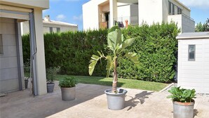 Un quartier résidentiel avec une terrasse dallée, des plantes en pot et une haie en arrière-plan.