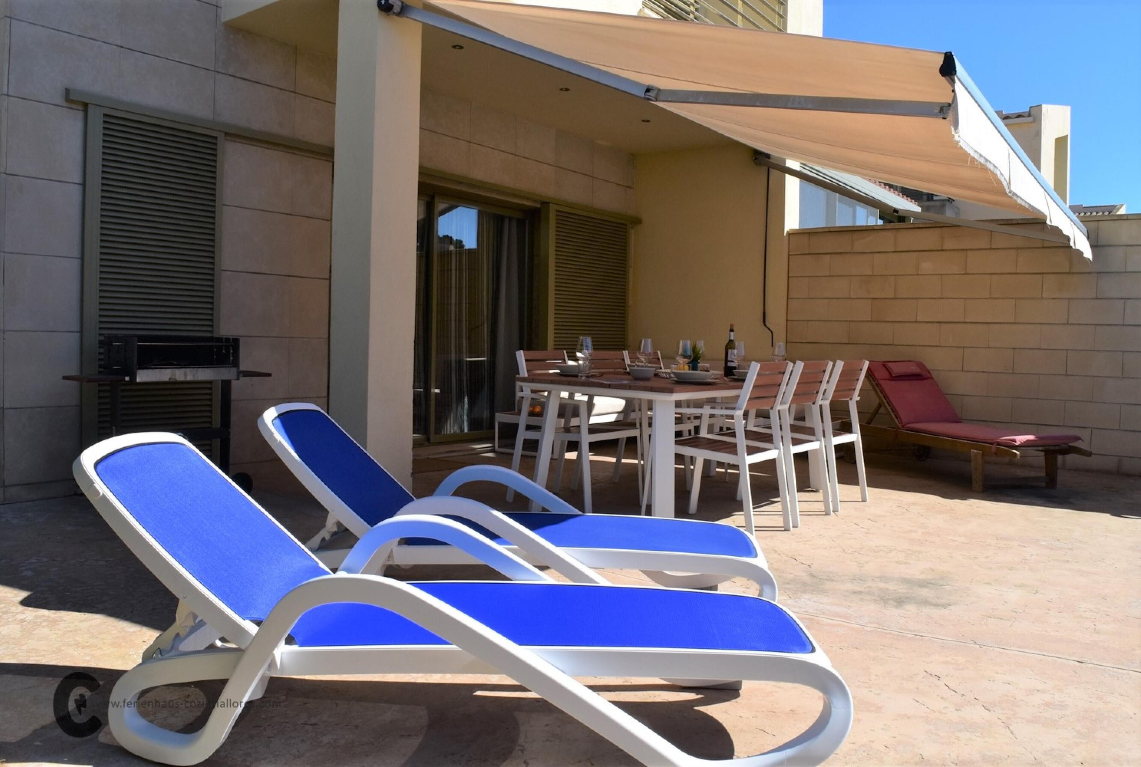 Un patio con una mesa lista para comer, sillas de descanso y una parrilla.