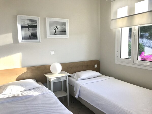 Quarto com duas camas, uma mesinha de cabeceira com abajur e duas fotos emolduradas na parede.