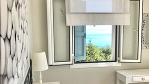 Un dormitori amb un llit, una tauleta de nit, una làmpada, una finestra amb vista al mar i una paret amb un disseny texturat.