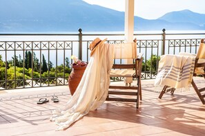 Terraço com vista para um lago e montanhas, com uma cadeira, uma toalha, um chapéu e um par de chinelos.