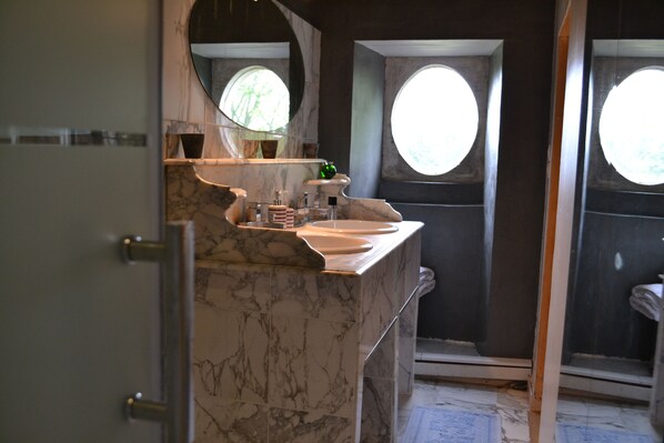 A bathroom with a marble sink, a large mirror, and two windows.