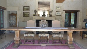 Un gran comedor con tapicería floral, rodeado por tres sillas. Se ve una chimenea con repisa al fondo.