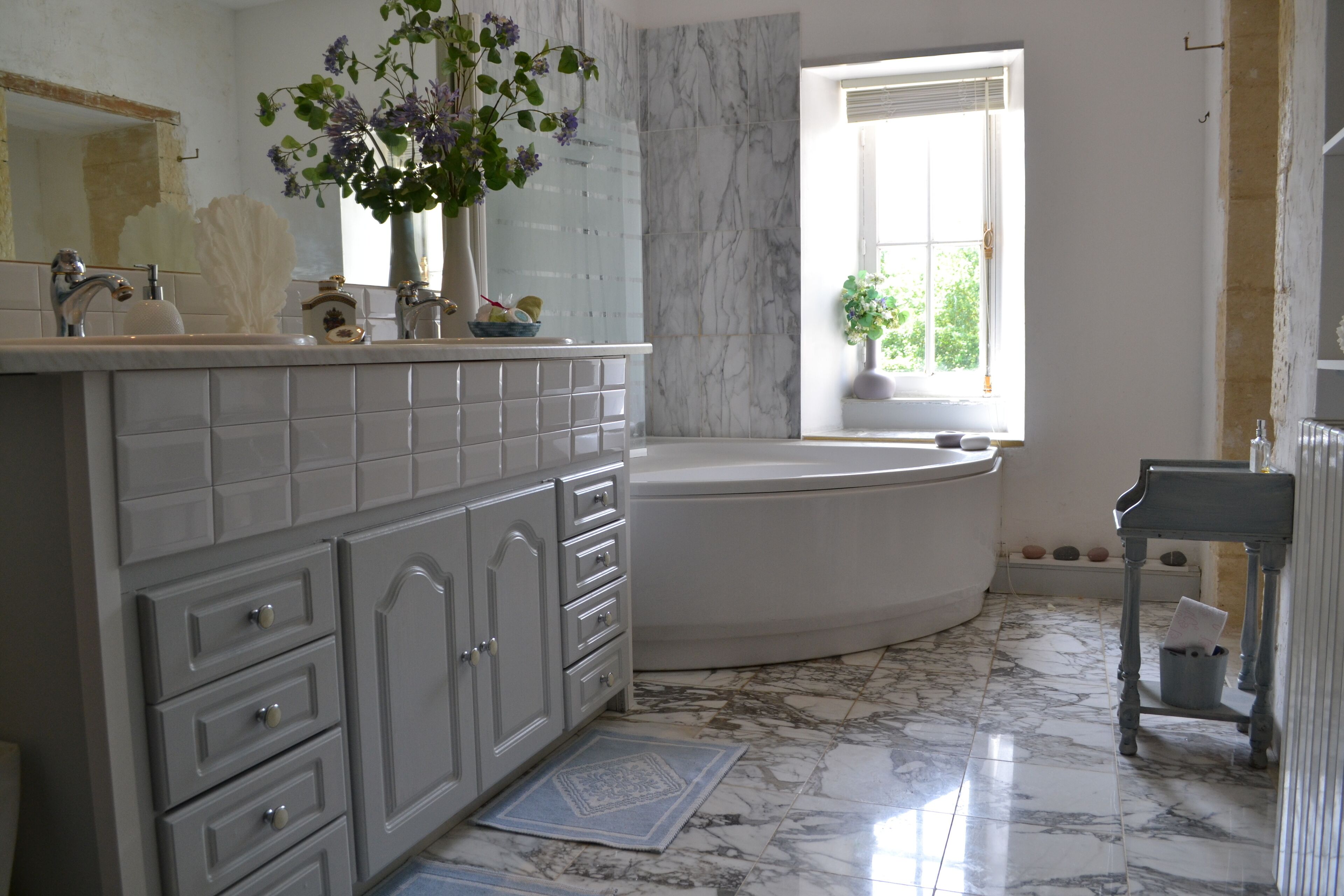 A bathroom with a white vanity, a bathtub, and a window with a view of greenery.