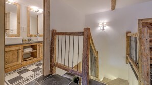Une salle de bain avec des poutres en bois, un sol carrelé, un escalier en bois et un miroir avec éclairage intégré.