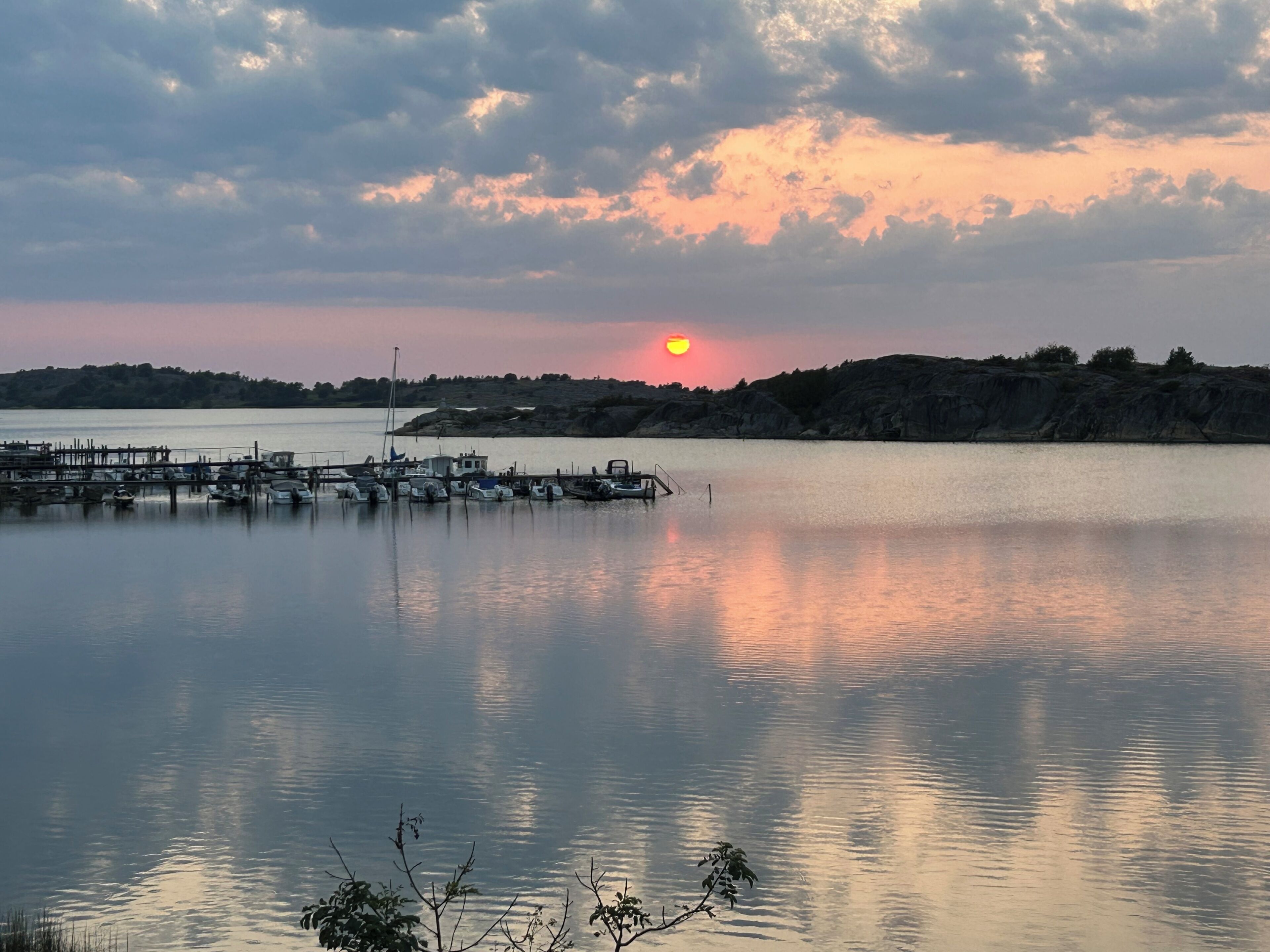 A calm body of water with a dock and boats, surrounded by hills and a sunset.