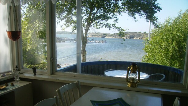 Zona pranzo con tavolo, sedie e vista su un lago con barche.