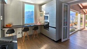 A modern kitchen with a large window, a stove, and two bar stools. - Apartment with balcony, direct beach access (Varenna)