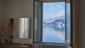 A room with a large window offering a view of a lake and mountains. - Apartment with balcony, direct beach access (Varenna)