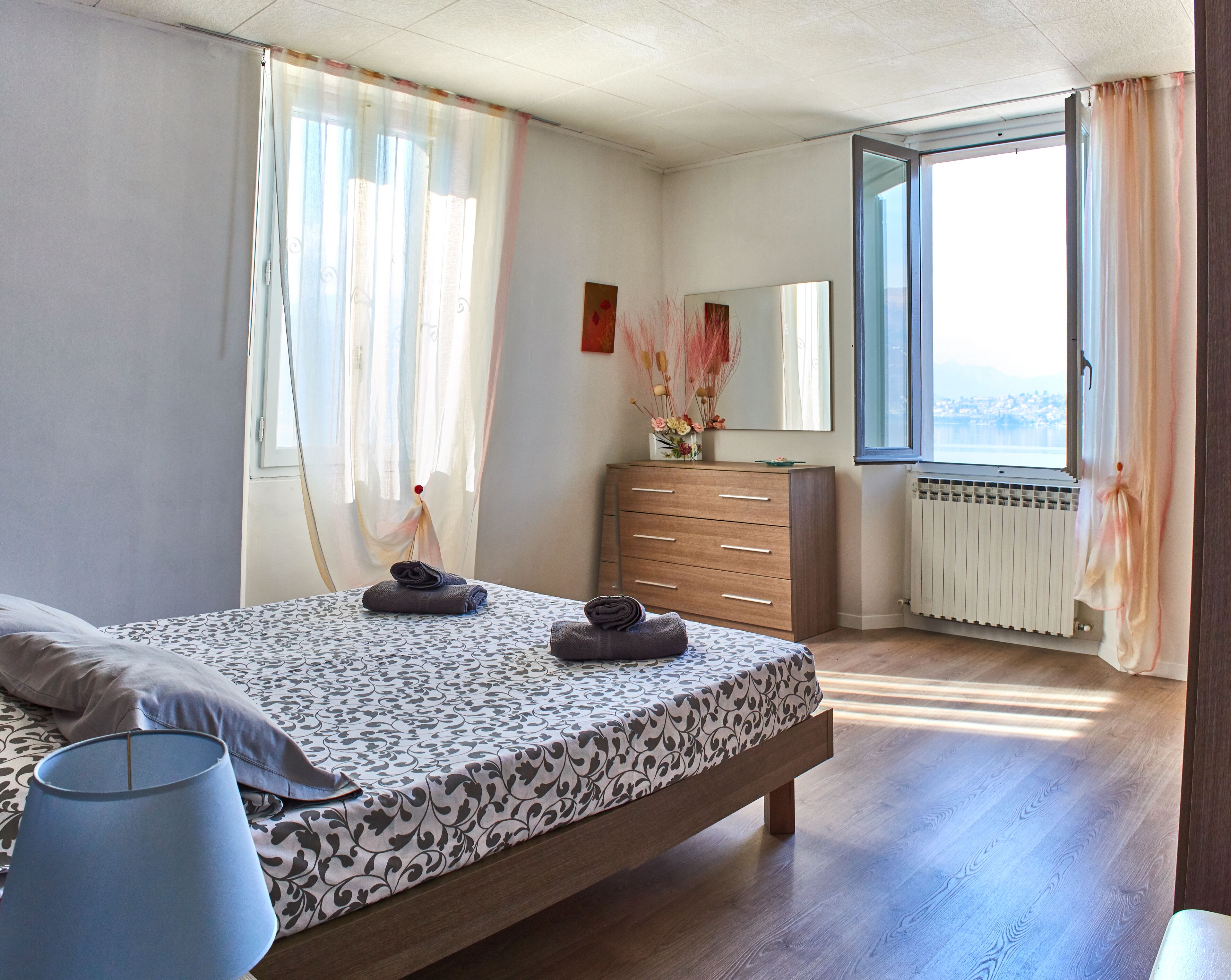 Une chambre à coucher avec un lit, une commode, une fenêtre avec des rideaux et un radiateur.