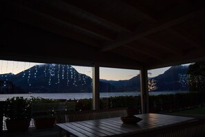 A terrace with a wooden table and chairs, overlooking a lake with mountains in the background. - Apartment with balcony, direct beach access (Varenna)