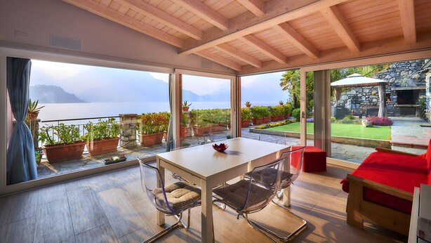 A modern room with a wooden ceiling, large windows, a table, and chairs. - Apartment with balcony, direct beach access (Varenna)