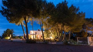 A modern house with a white exterior, surrounded by tall trees and a well-maintained garden. - Casa Rosita, free Wifi, 75 meters from the Niu Blau beach, ideal families. (Santa Eulalia del Rio)