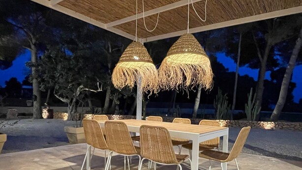 An outdoor dining area with a long table and chairs, surrounded by a thatched ceiling and trees. - Casa Rosita, free Wifi, 75 meters from the Niu Blau beach, ideal families. (Santa Eulalia del Rio)