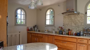 Une cuisine avec des meubles en bois, un plan de travail en marbre et deux fenêtres en arc de cercle.
