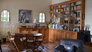 Un salon spacieux doté d’une cheminée, d’une grande bibliothèque en bois et d’un coin repas avec une table ronde et des chaises.