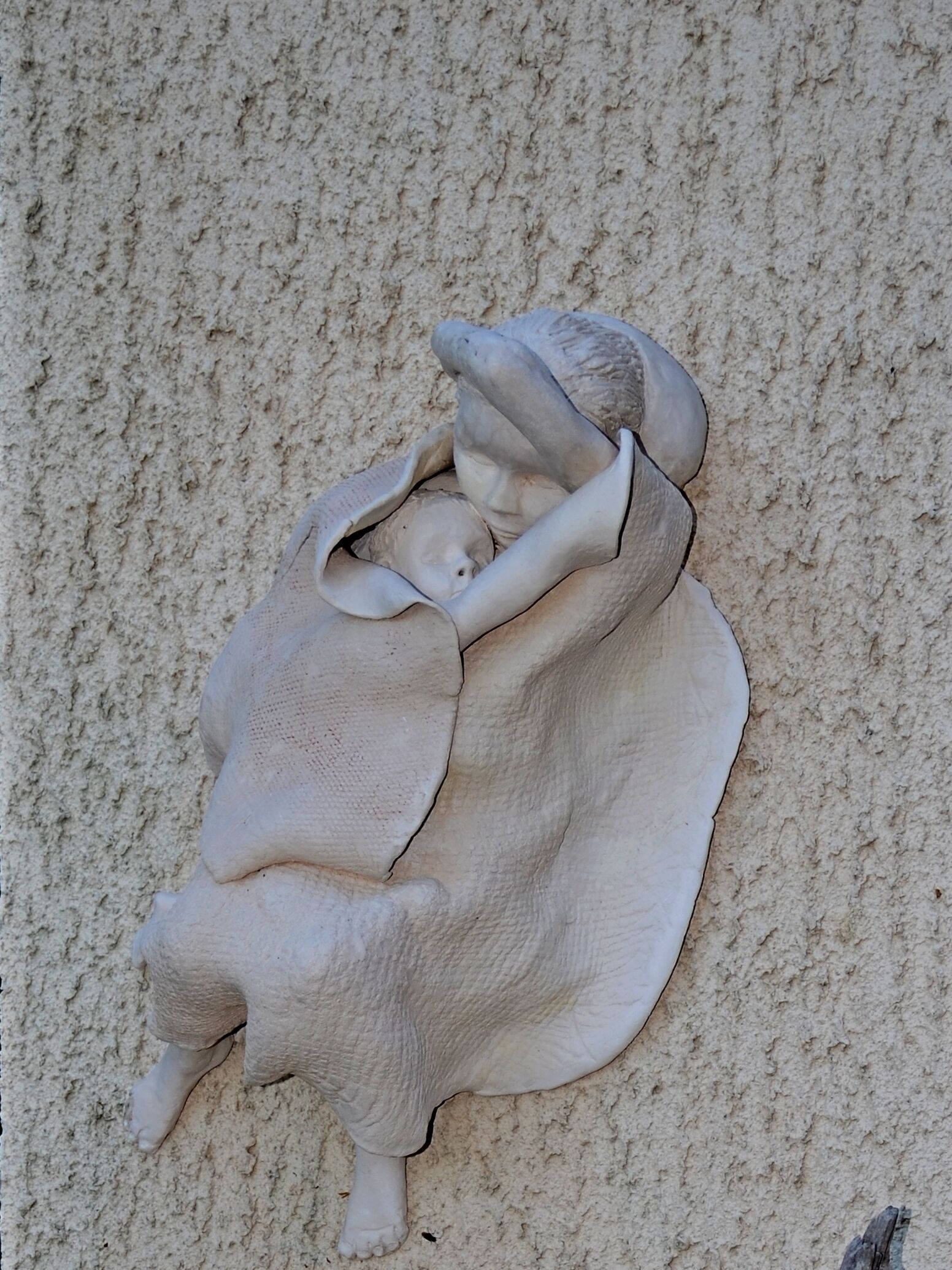 Une sculpture représentant une figure allongée, adossée à un mur à la texture particulière.