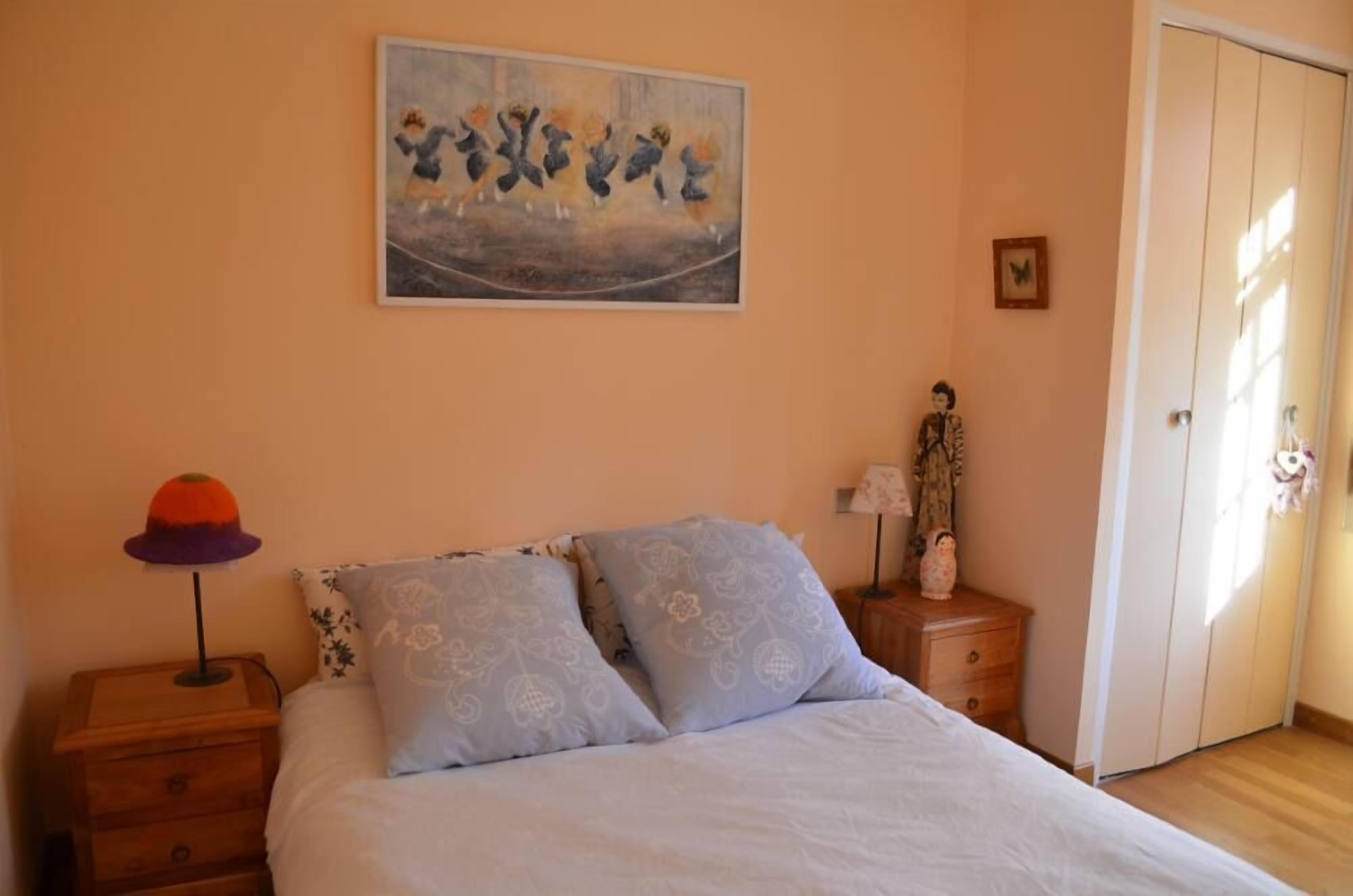 A bedroom with a bed, a nightstand, a lamp, a dresser, a wardrobe, and a painting on the wall.