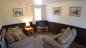 A living room with two grey sofas, a small table with a lamp, a television, and framed pictures on the walls. - Birchenfields Family Friendly Cottages, Play Barn for all Ages and Summer Hous (Stoke-on-Trent)