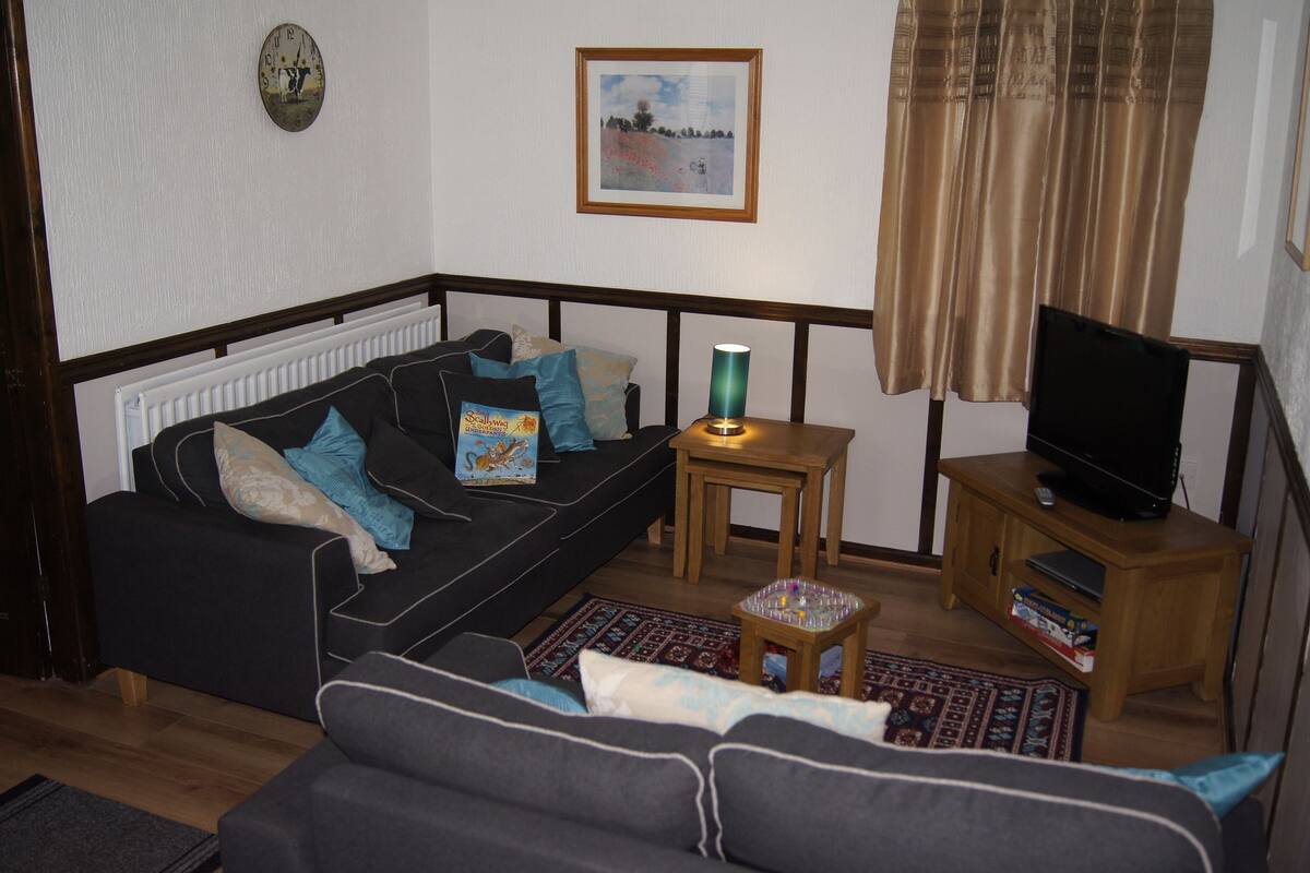 A living room with a sofa, a small table with a lamp, a television on a wooden stand, and a framed picture on the wall.