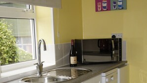 A kitchen with a stainless steel sink, a stove, and a microwave. There is a window above the sink, and a painting on the wall. - Birchenfields Family Friendly Cottages, Play Barn for all Ages and Summer Hous (Stoke-on-Trent)