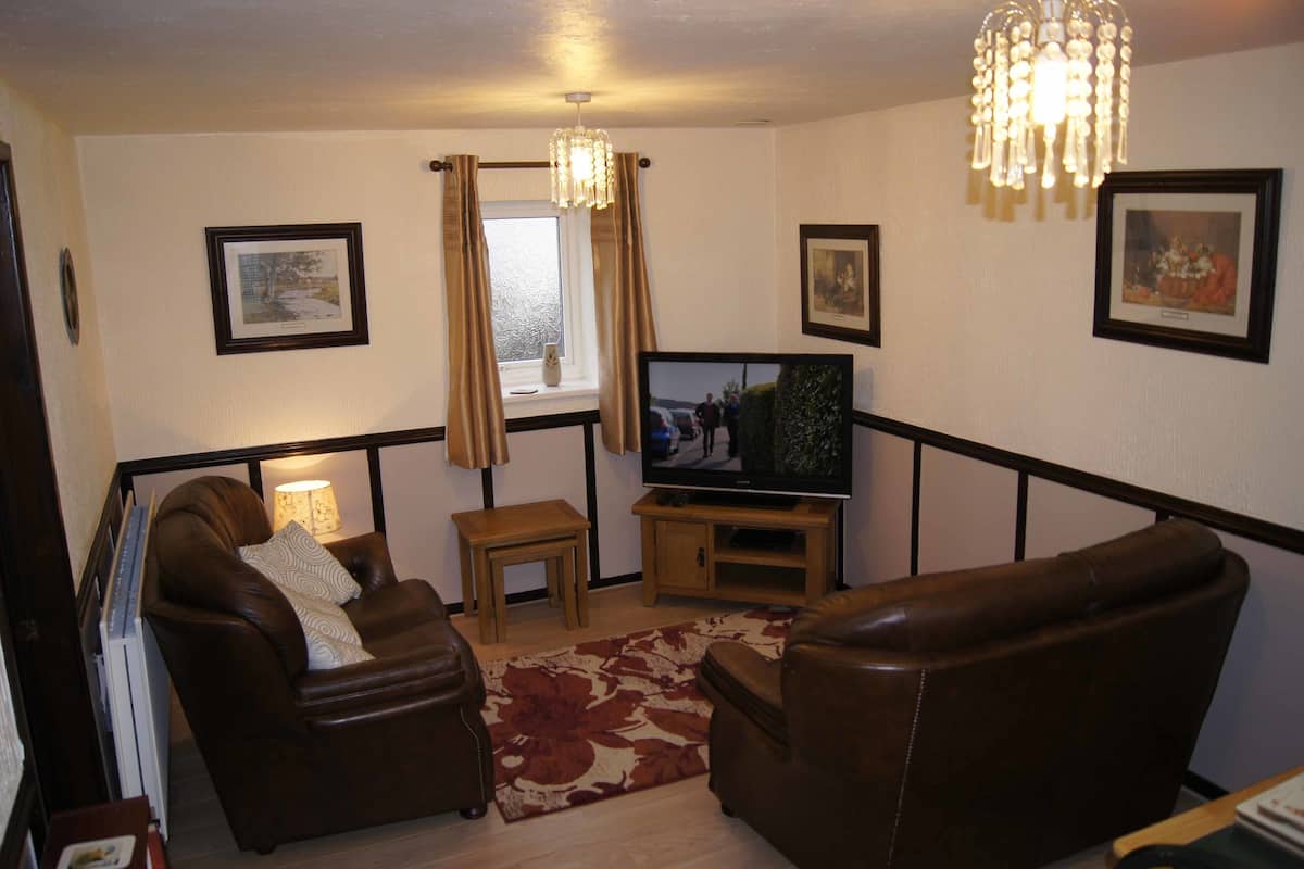 A living room with two leather sofas, a television, a small table, and a chandelier.