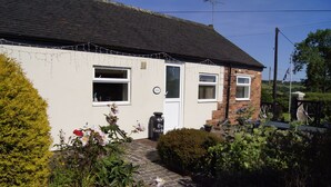 A two-story house with a white exterior, a brick section on the right, and a garden with various plants and flowers. - Birchenfields Family Friendly Cottages, Play Barn for all Ages and Summer Hous (Stoke-on-Trent)