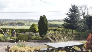 A garden with a picnic table, a stone wall, and a view of a rural landscape. - Birchenfields Family Friendly Cottages, Play Barn for all Ages and Summer Hous (Stoke-on-Trent)