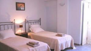 A bedroom with two beds, each with a white bedspread and pillows, a bedside lamp, and a framed picture on the wall. - Riverside apartment with private pool in old town - WiFi (Tavira)