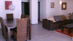 A living room with a dark brown sofa, a dining table with chairs, and a red rug. - Riverside apartment with private pool in old town - WiFi (Tavira)