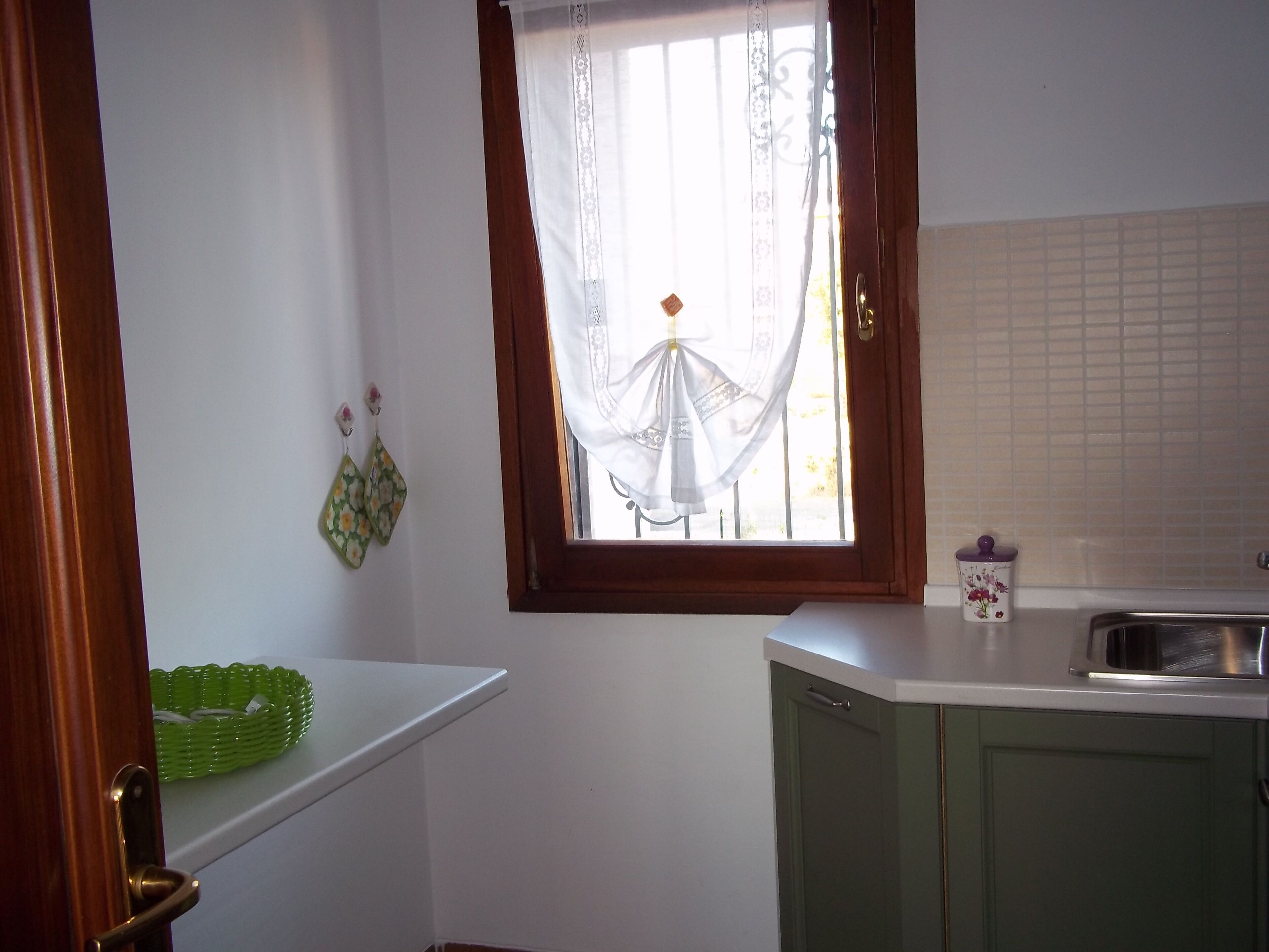 Eine Küche mit Fenster, einem grünen Schrank, einer weißen Arbeitsplatte und einem grünen Korb.