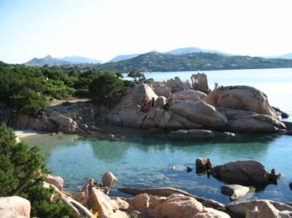 Un paisaje costero con grandes rocas, agua cristalina y montañas a lo lejos.