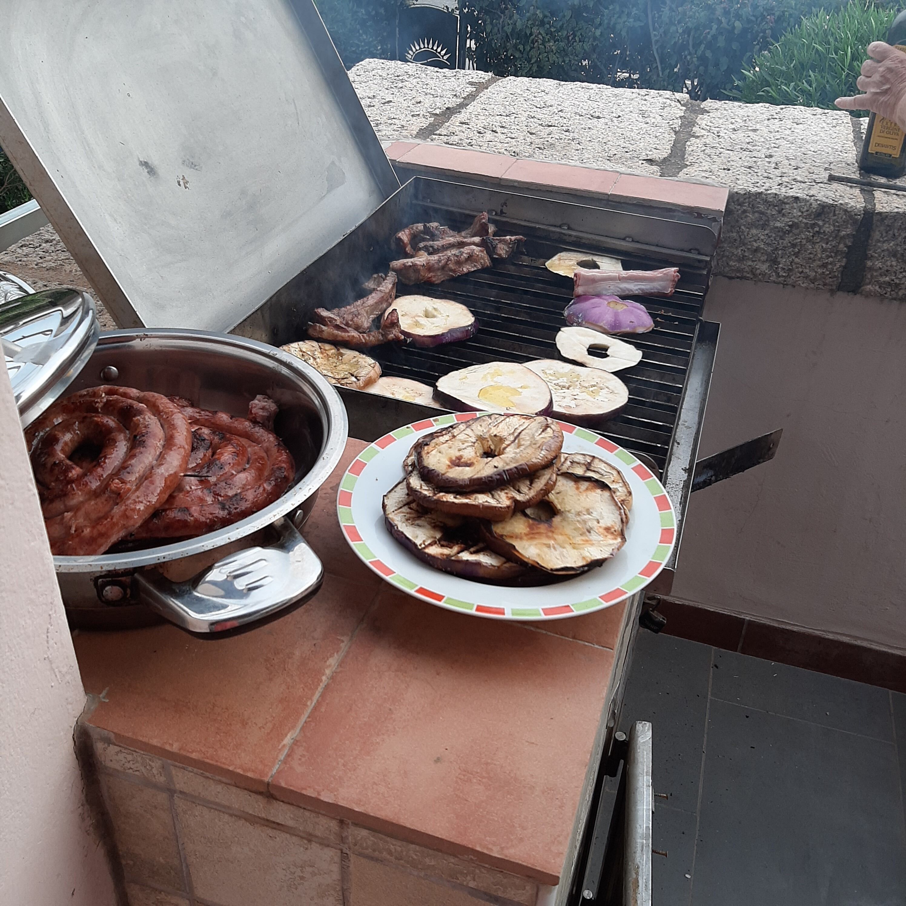 Uma churrasqueira ao ar livre com diversos carnes e legumes sendo preparados.
