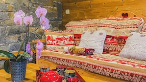 A cozy room with a stone wall, wooden ceiling, and a sofa with patterned cushions.