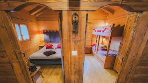 A wooden cabin with a bed, a bunk bed, and a small table.