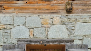 A rustic stone building with wooden shutters and a window displaying a bouquet of flowers.